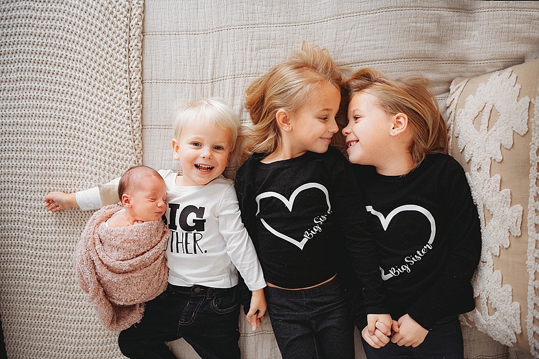 siblings laughing with newborn baby with heart and big brother shirt