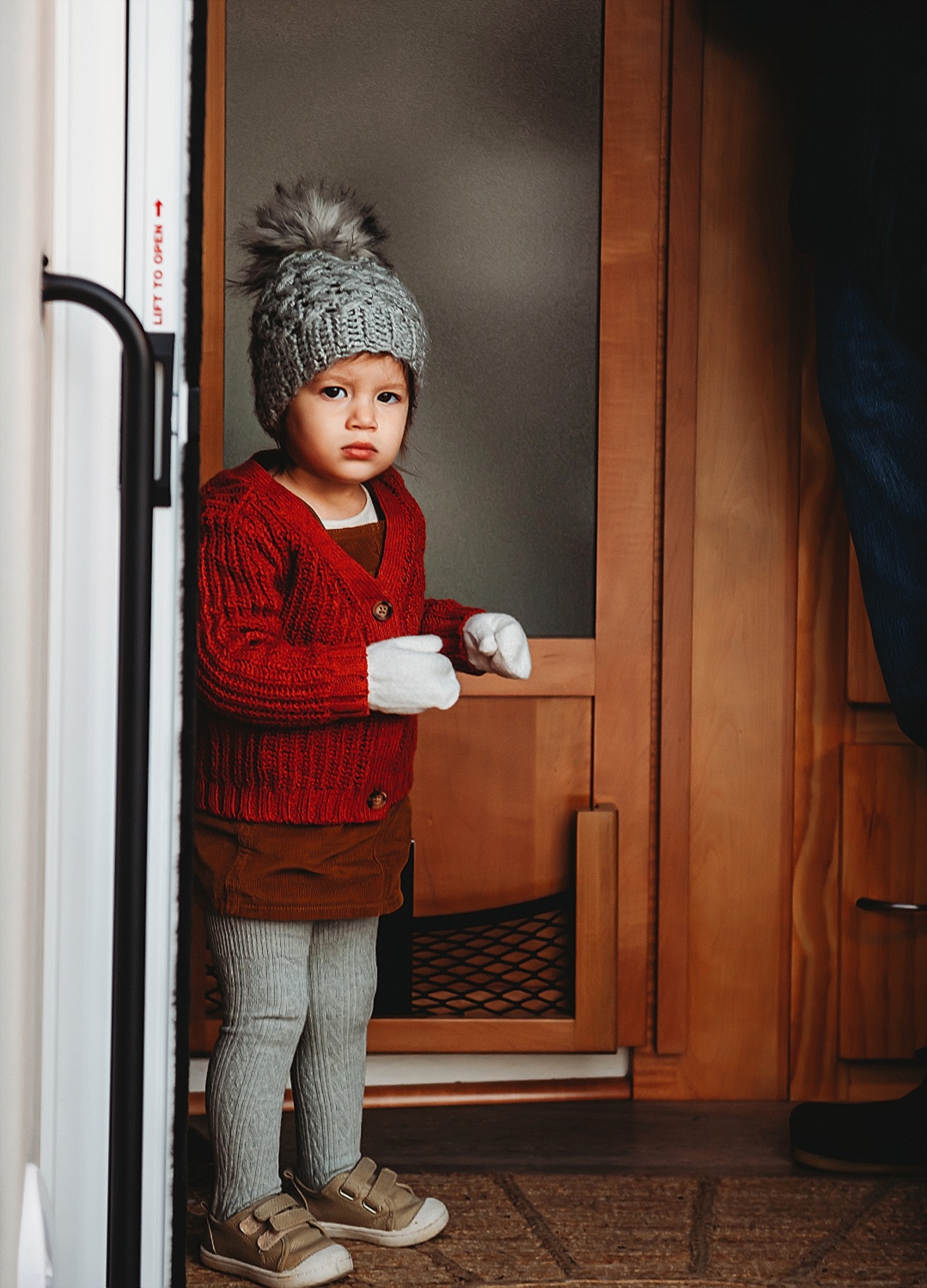 young girl in hat and mittens frowning at camera