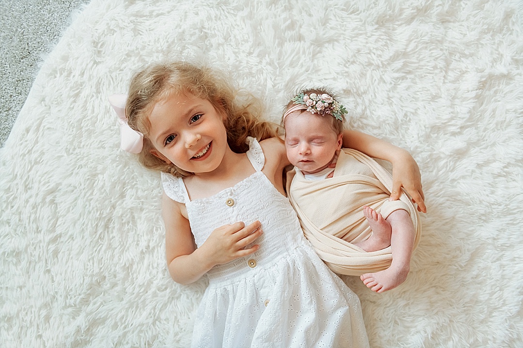 big sister in white smiling with newborn sister for her newborn photography session with siblings in Annapolis MD