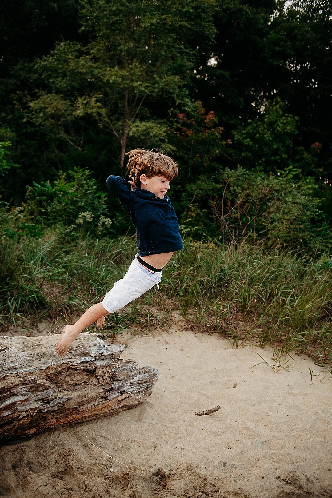 boy in blue shirt and white pants jumping off a log