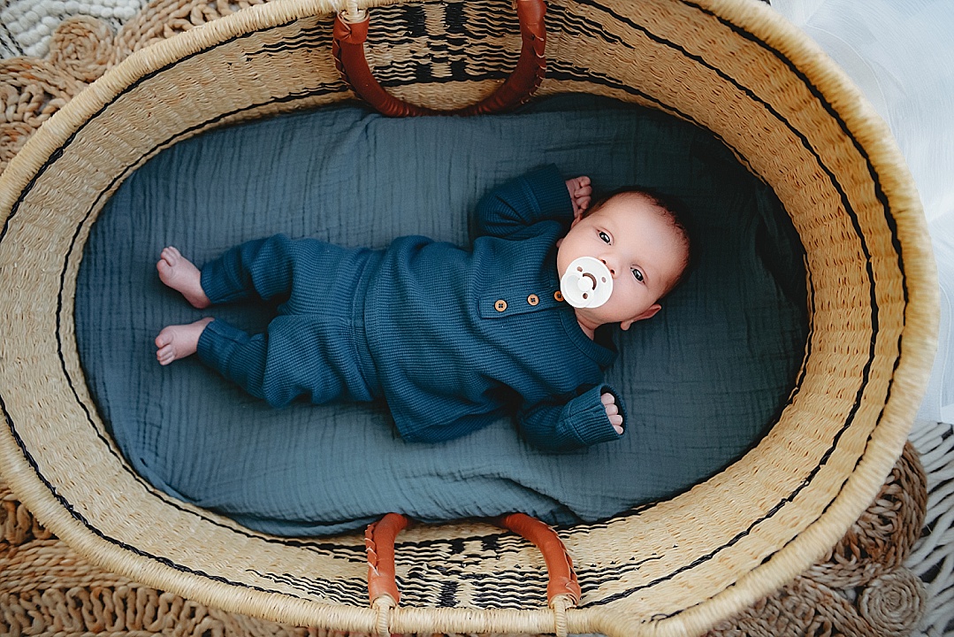 baby wearing blue with pacifier in moses basket