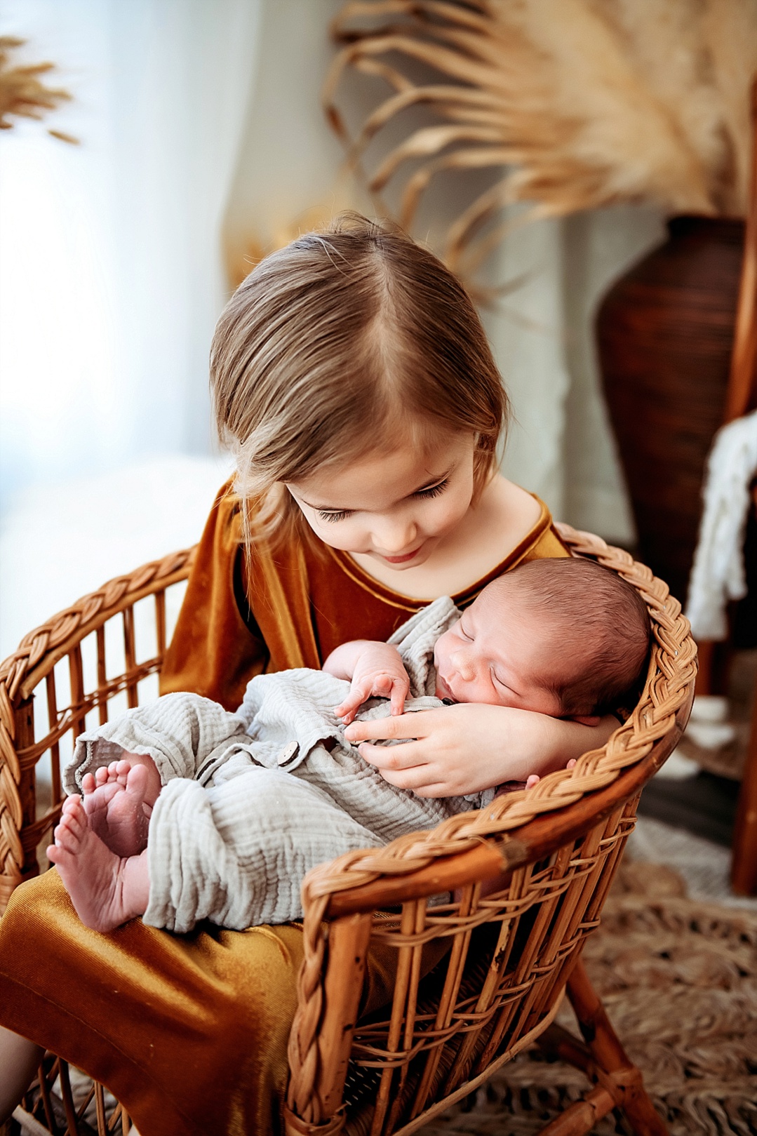 big sister where a rust dress holding newborn baby in Kent Island newborn photography session